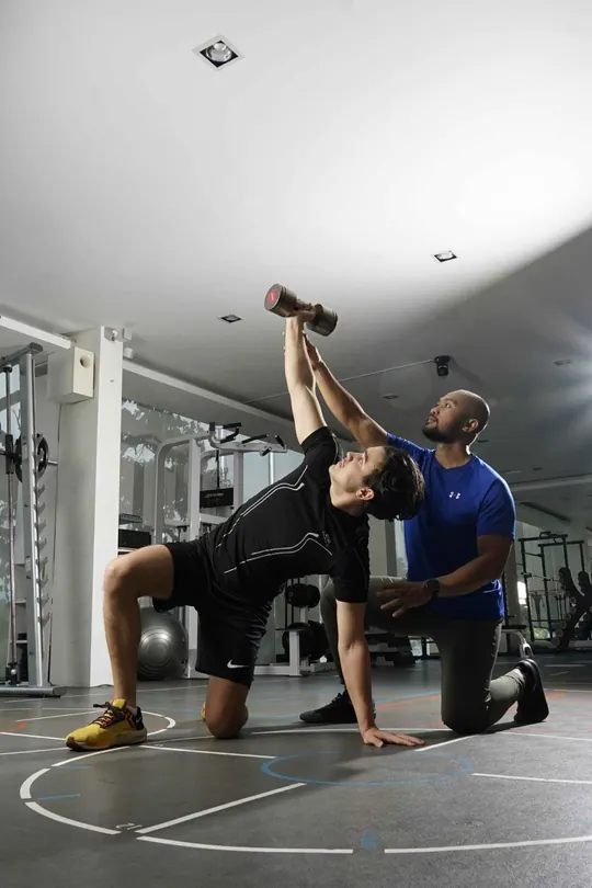 Personal trainer mendampingi klien berlatih dengan dumbbell di private gym BodySoul